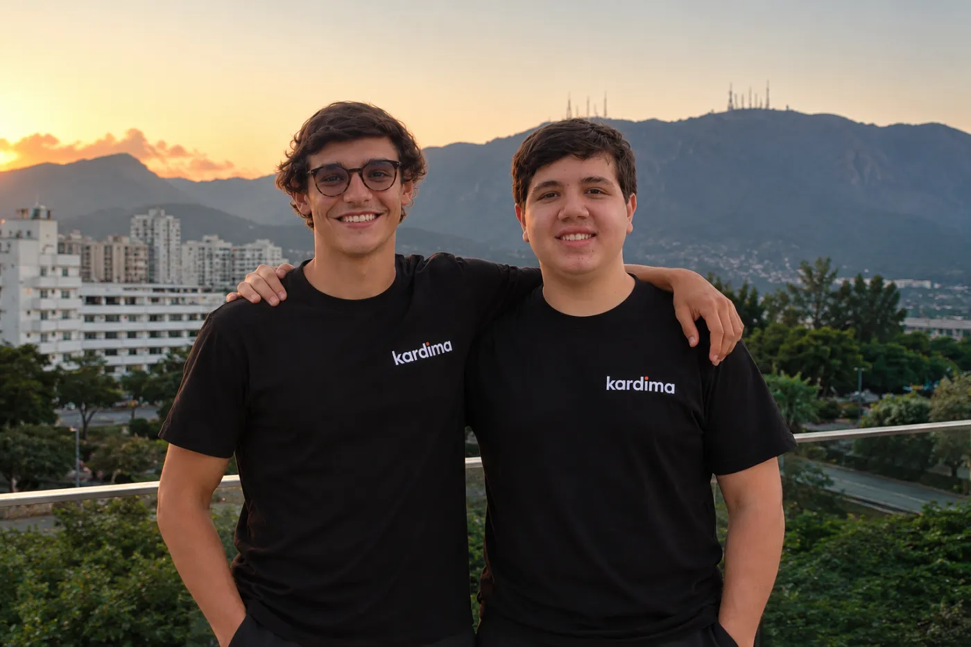 Os dois fundadores da Kardima, com camisetas da marca, em uma varanda ao entardecer